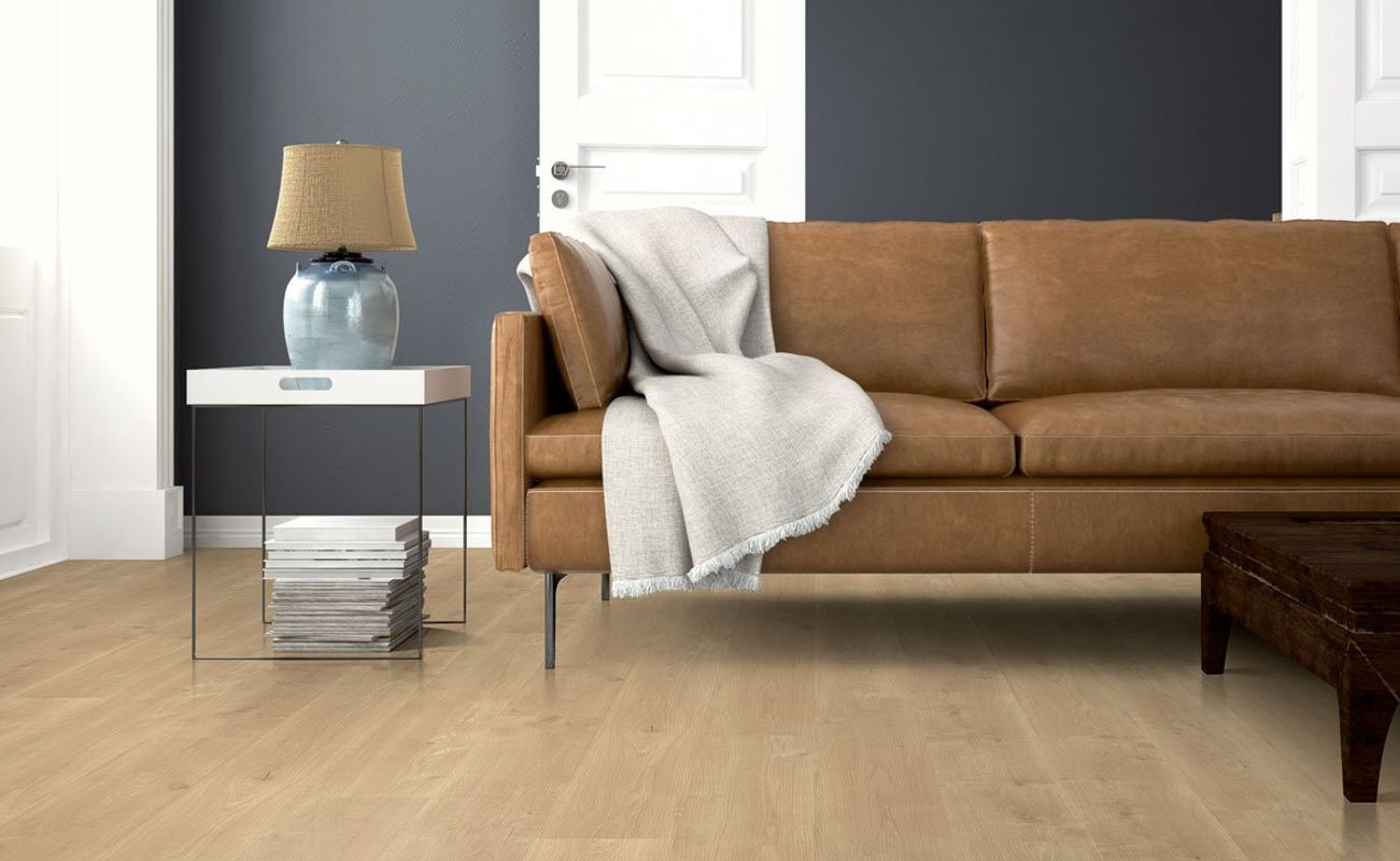Ein Wohnzimmer mit einem braunen Ledersofa, einem Tisch mit einer Lampe und einem Regal mit Zeitschriften. Wände in Grau und Weiß.